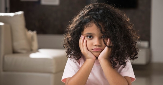 young girl with dark curly hair looking sad
