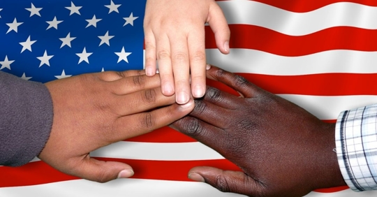 three hands stacked on each other with a United States flag in the background