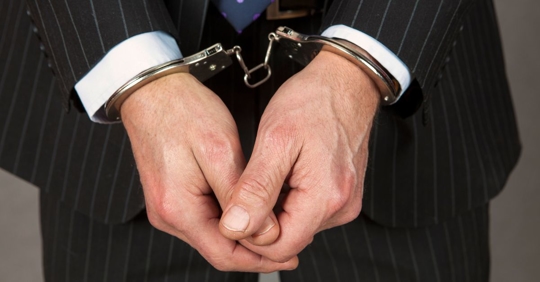 man wearing a suit holding his hands together while wearing handcuffs