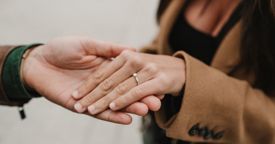 close up of a woman wearing an engagement ring, her hand is being held by a man's hand