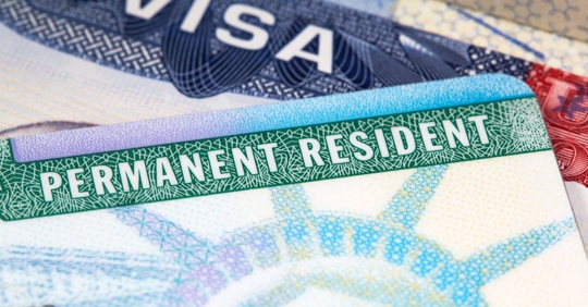 close up of a Green Card and visa card stacked on a desk