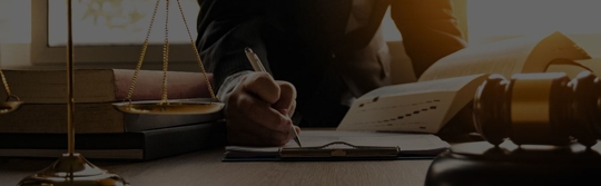 person writing on desk with scale and gavel