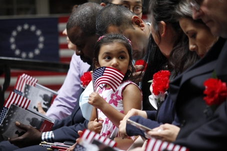The daughter of a immigrant holds an American flag while she joins her mother's naturalization ceremony