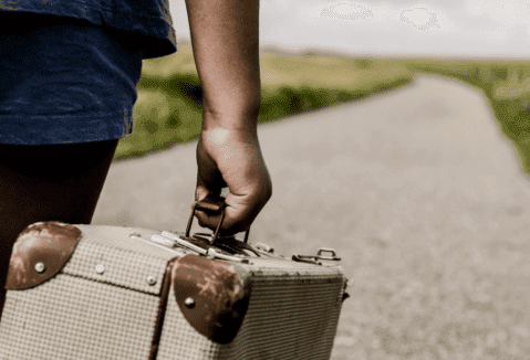 man holding suitcase walking down a paved road