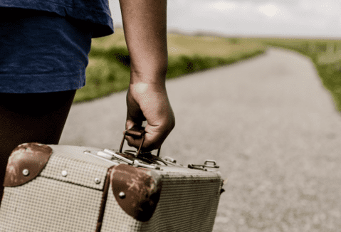 man holding suitcase walking down a paved road